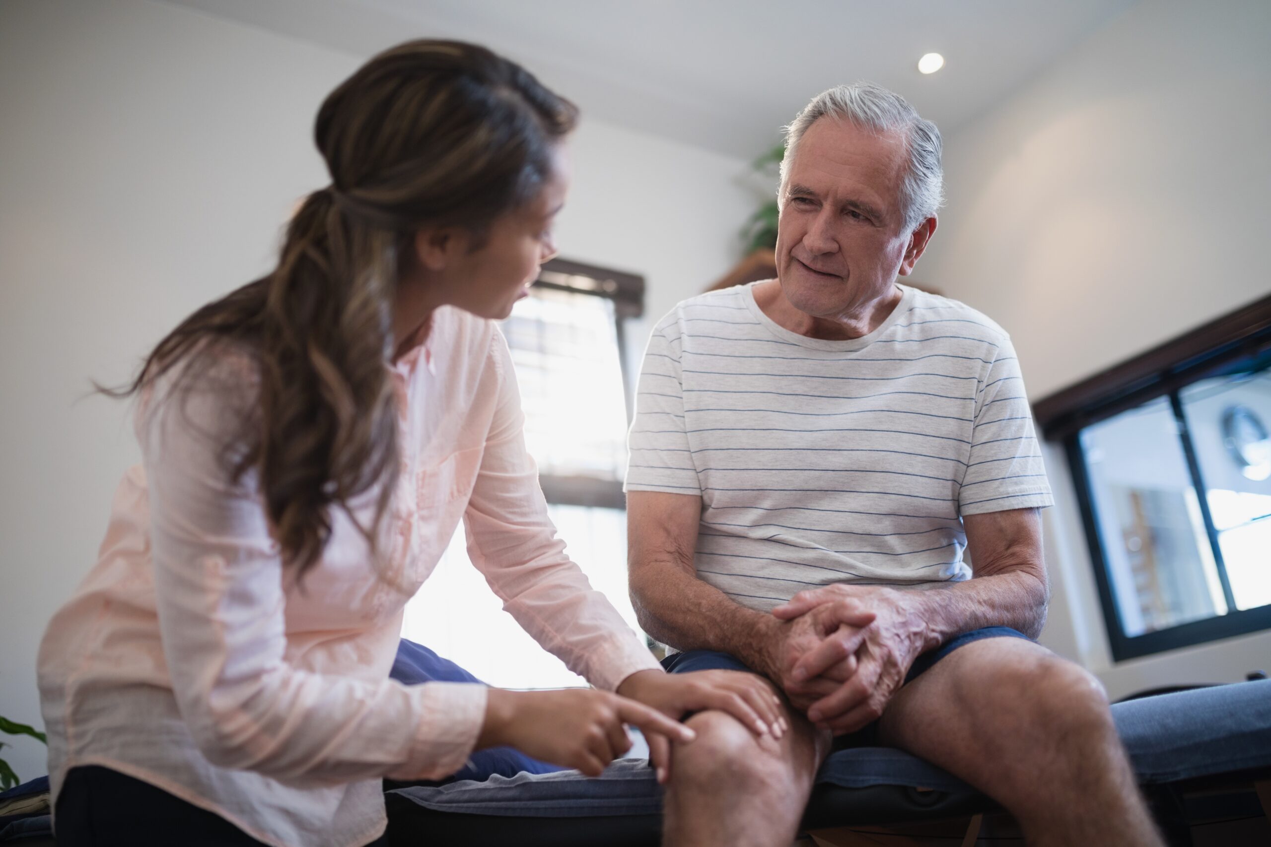 Low angle view of female therapist pointing at knee while male patient listens 