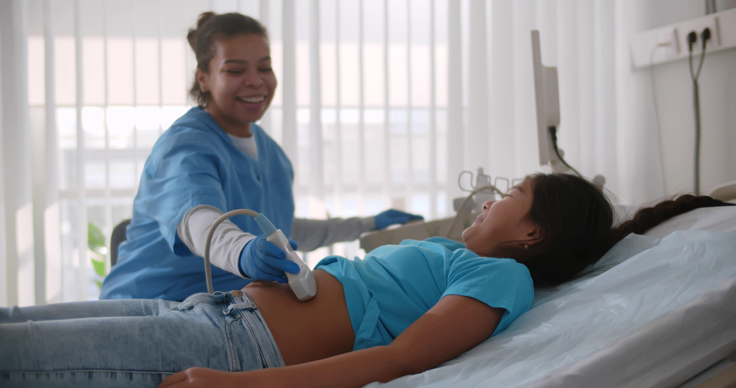 Ultrasound technologist using transducer on young patient's stomach for abdominal ultrasound.