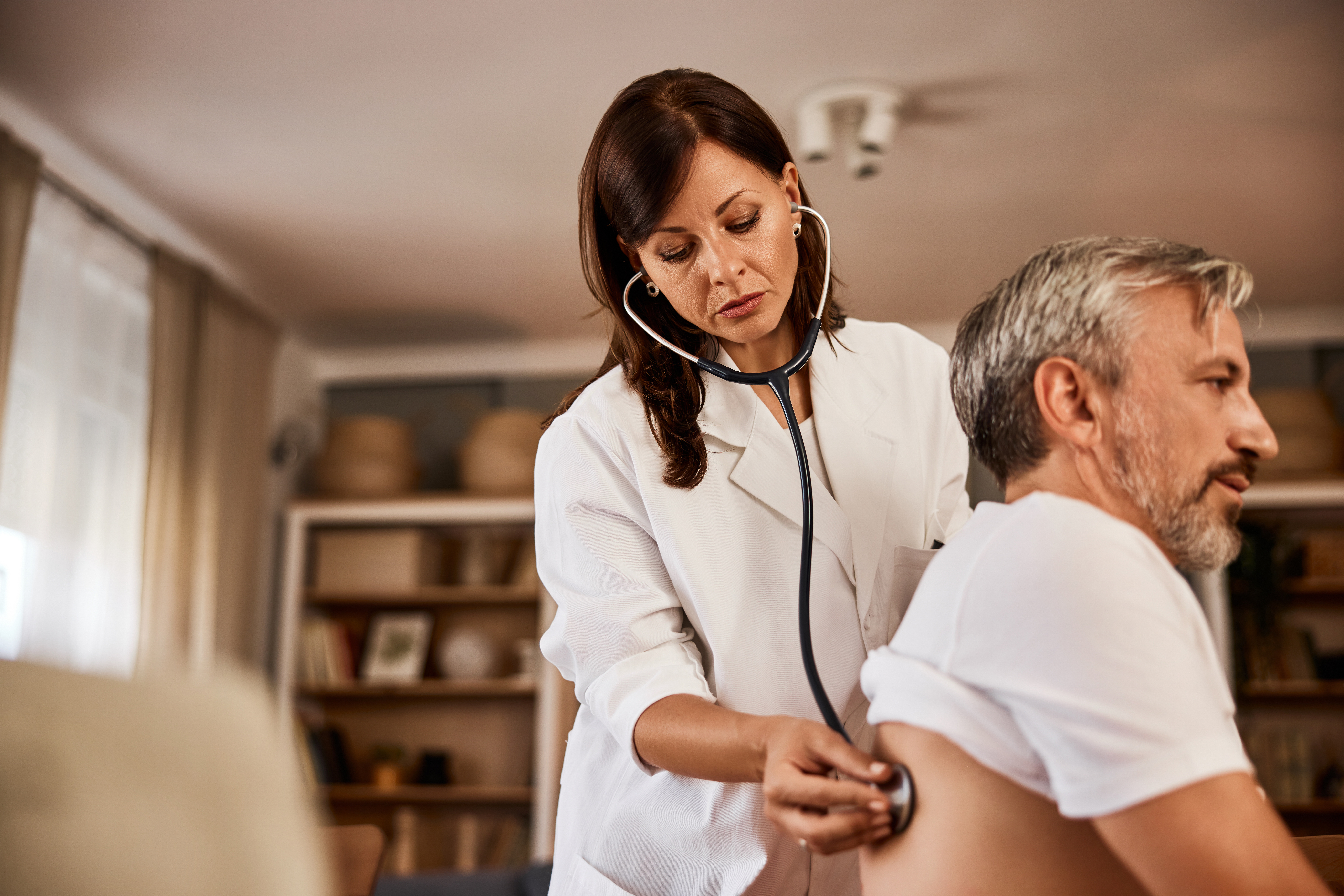 Serious doctor checking up lungs of a mature male patient.